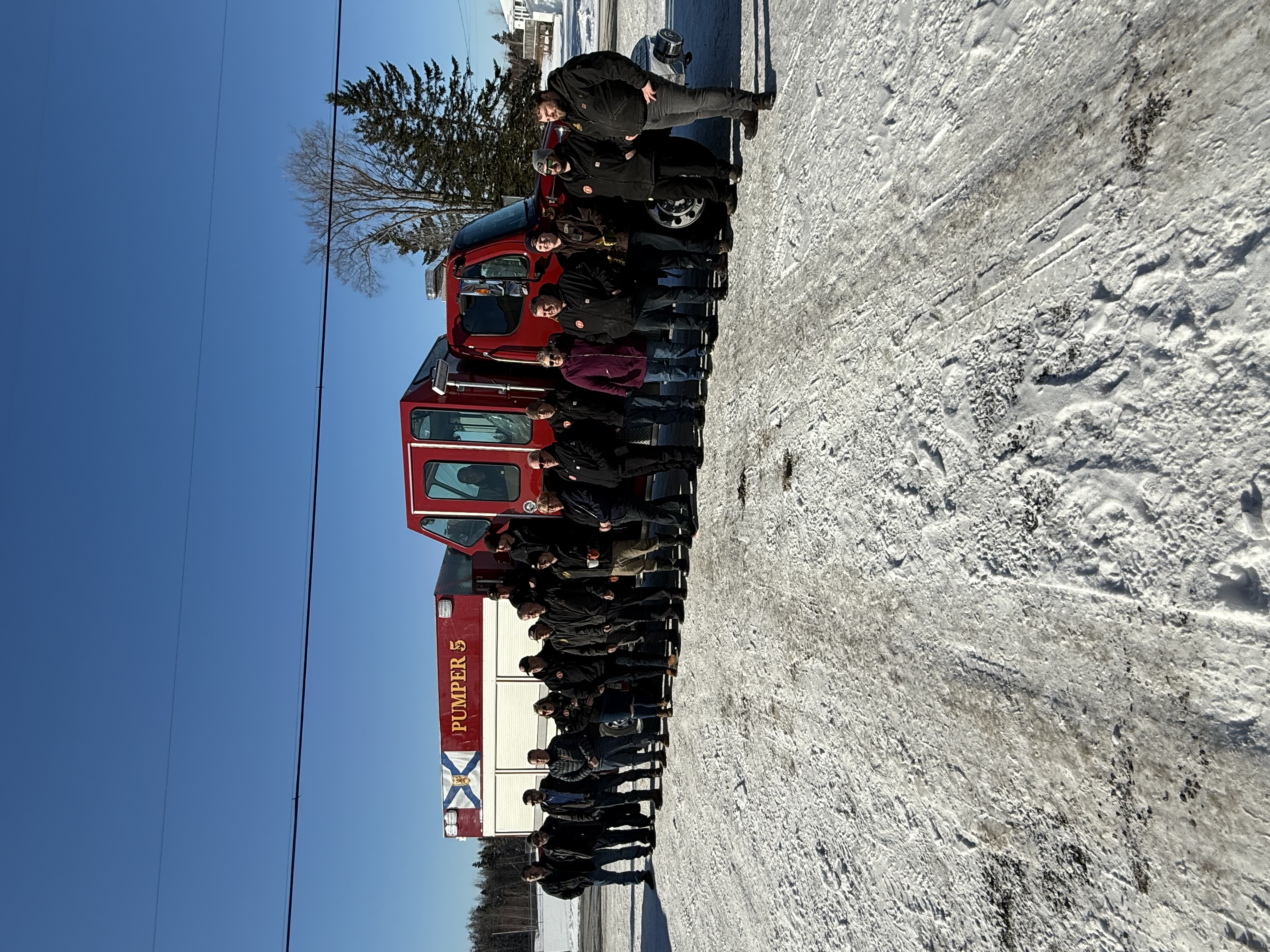 A red truck sits in a snow-covered parking lot with a large group of people standing in front of it.