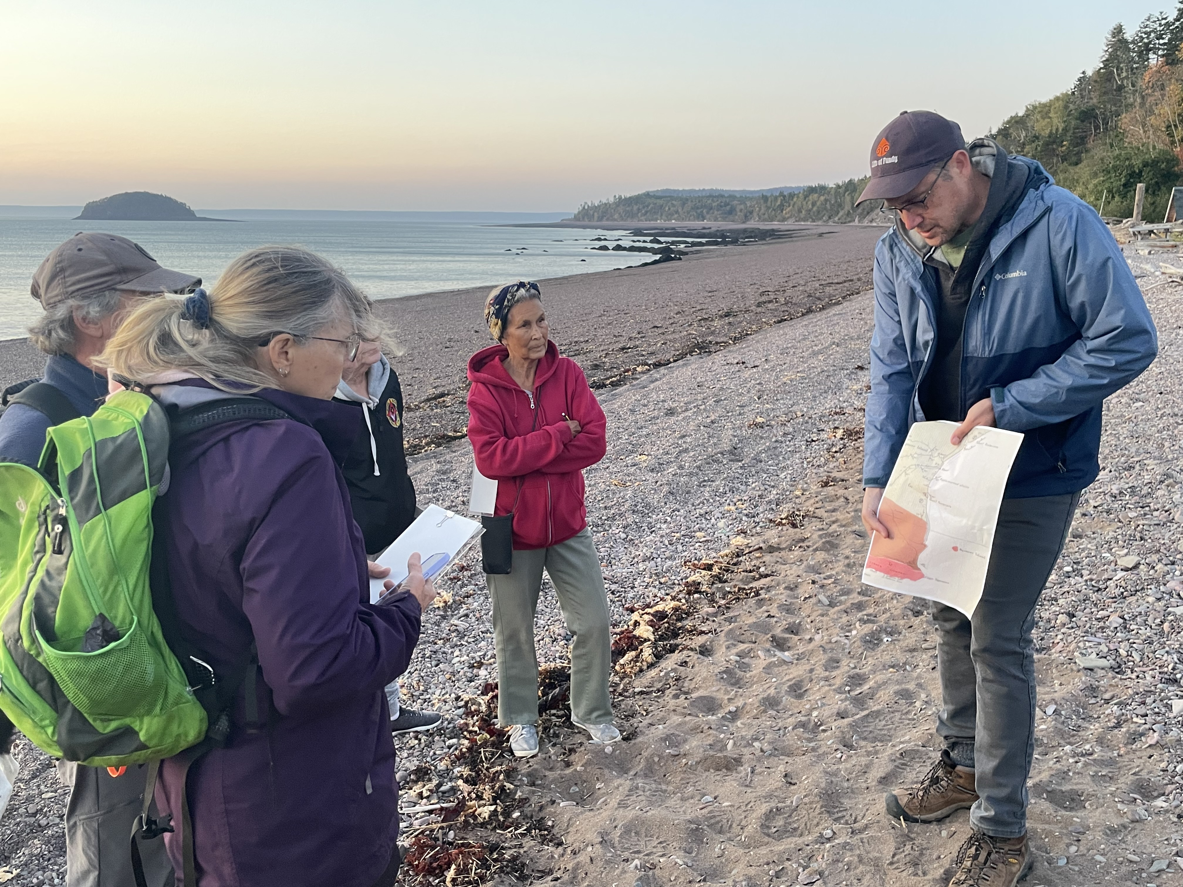 A group of people on the left watch as a man describes the geological history of Spencer's Island beach.