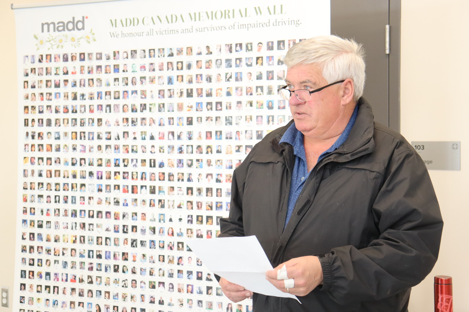A man reads a proclamation while standing in front of a MADD Canada poster that shows photos of victims of impaired driving. 