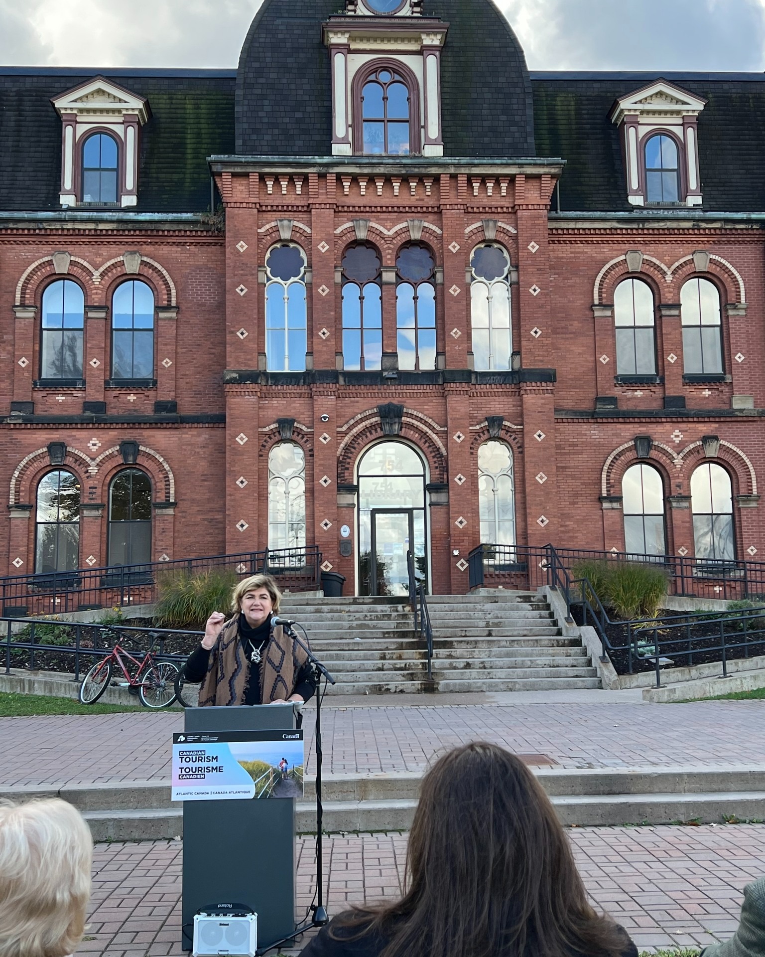 A woman stands at a podium in front of a building