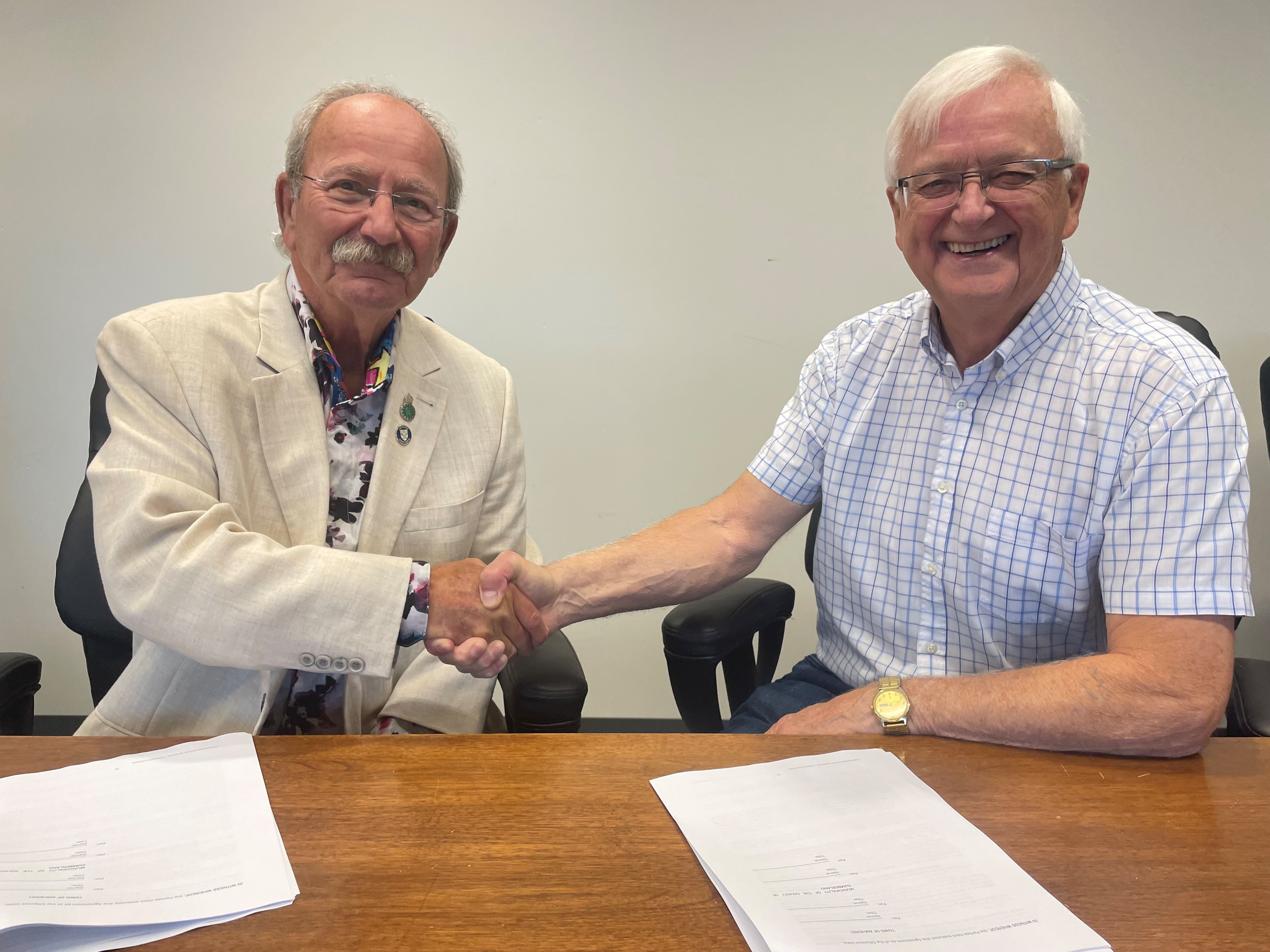 Two men shake hands while seated at a table.