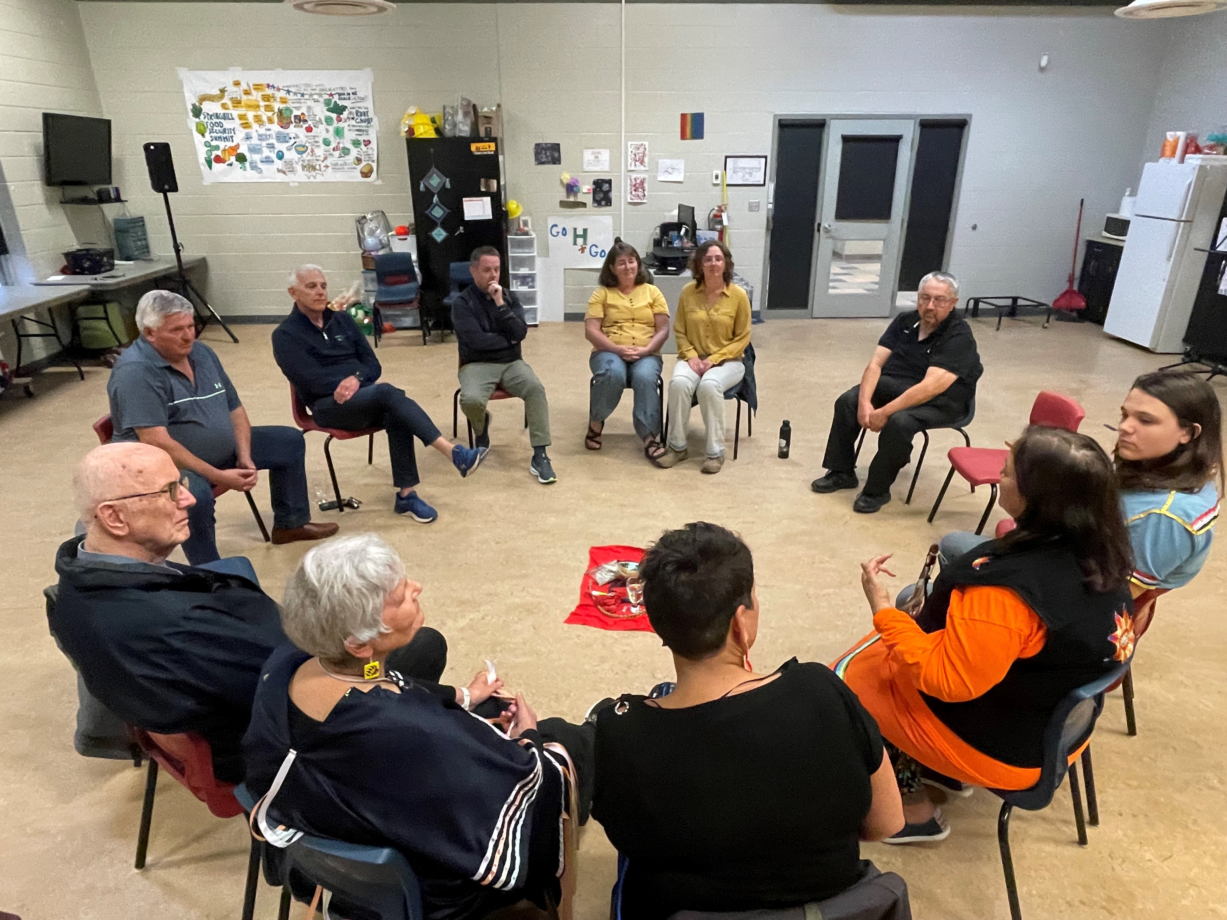 A group of people sit in a circle around a display of Mi'kmaw items.