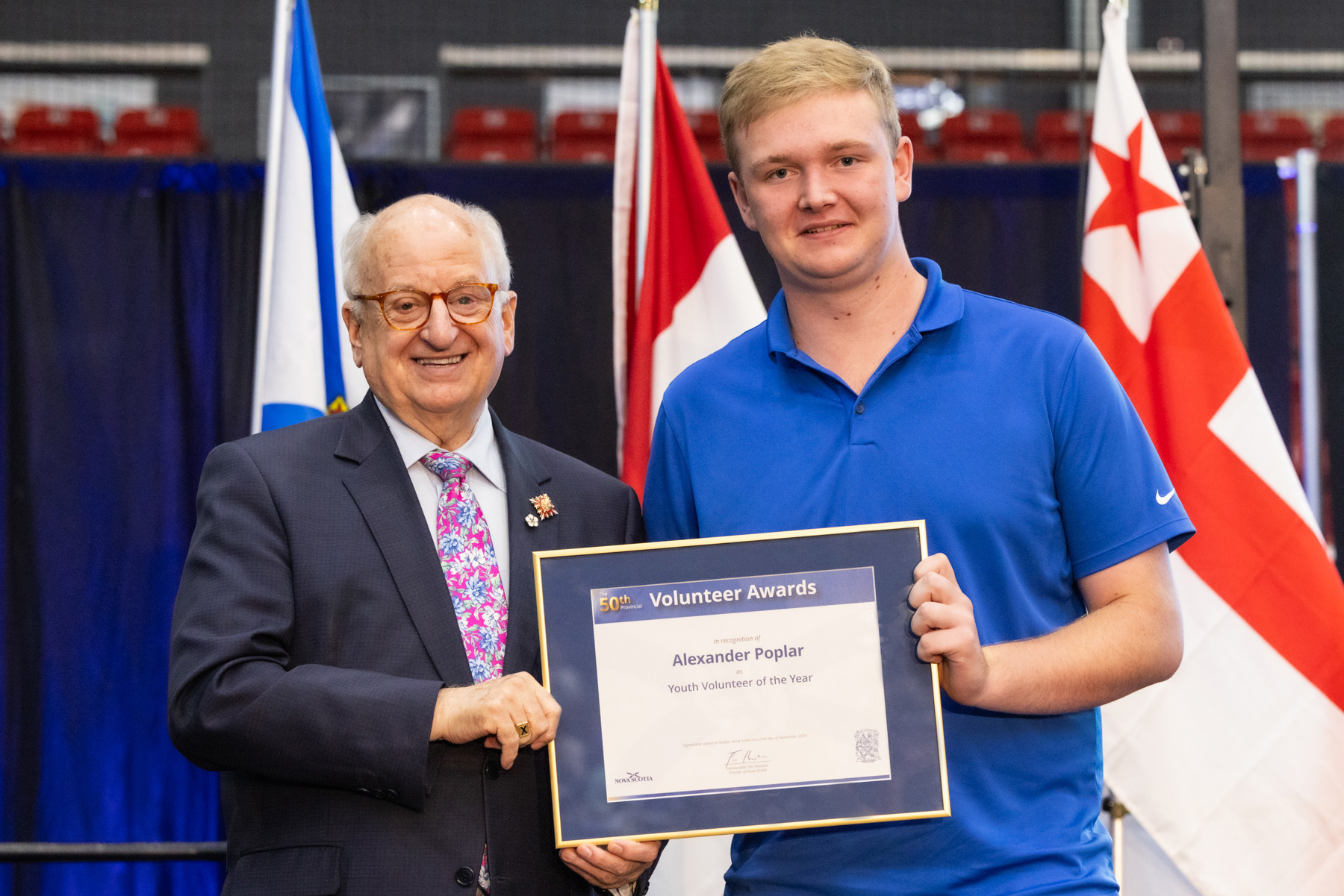 Two men with a certificate stand in front of three flags