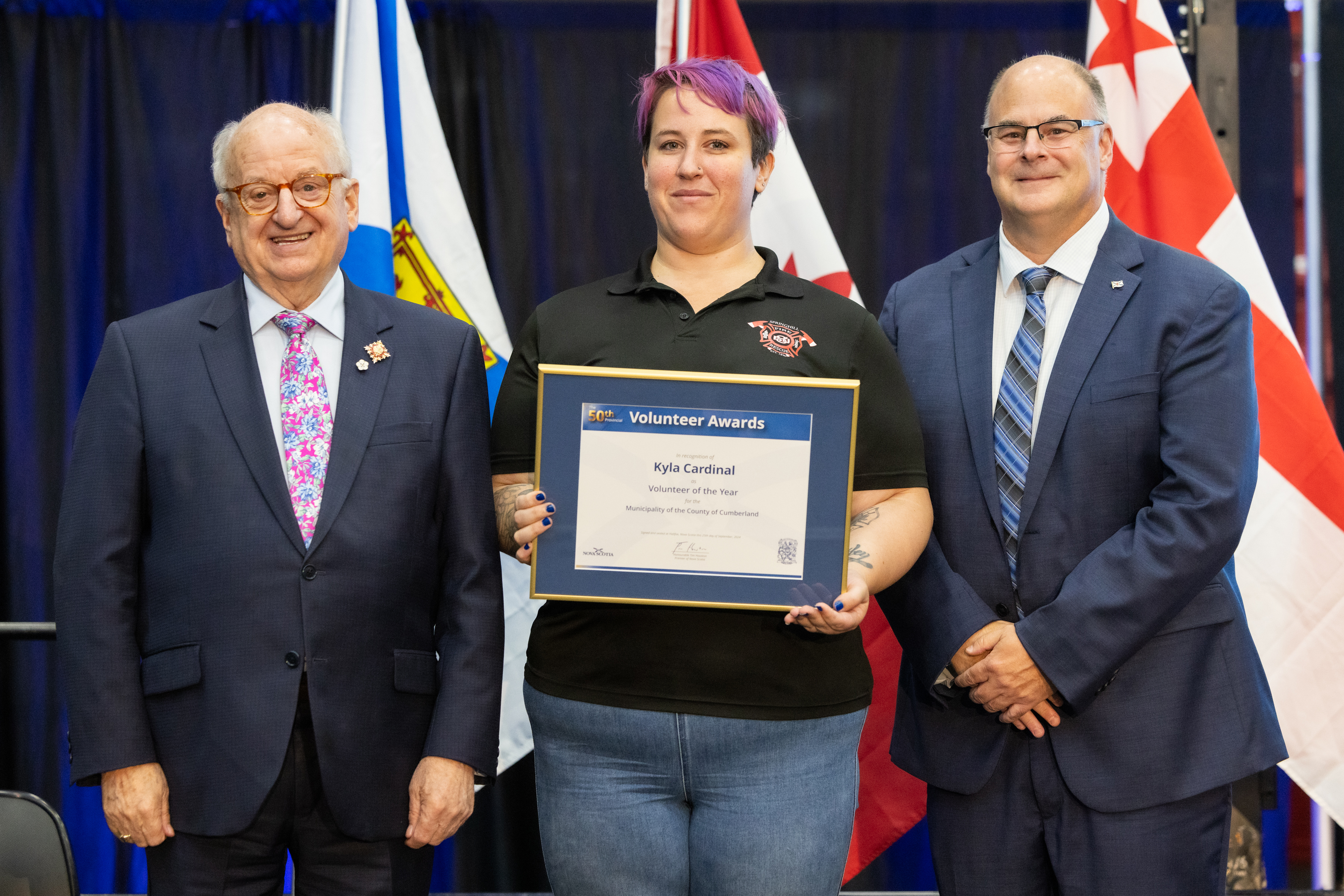 A woman and two men stand with a certificate in front of three flags